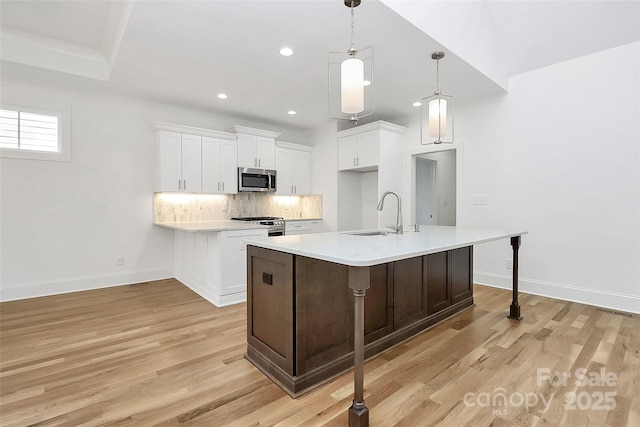 kitchen featuring backsplash, appliances with stainless steel finishes, light wood-style floors, and a sink