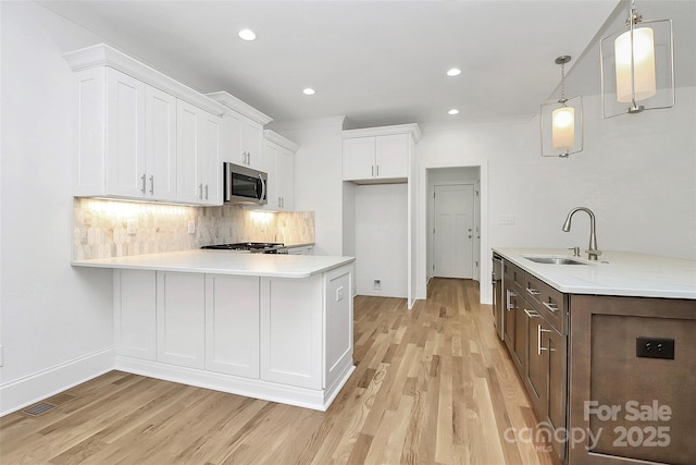 kitchen featuring a sink, light countertops, white cabinets, stainless steel microwave, and tasteful backsplash