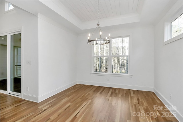 unfurnished dining area featuring an inviting chandelier, a raised ceiling, and light wood-style flooring