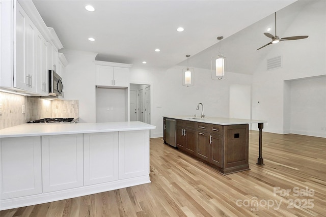 kitchen with light countertops, a peninsula, white cabinets, stainless steel appliances, and a sink