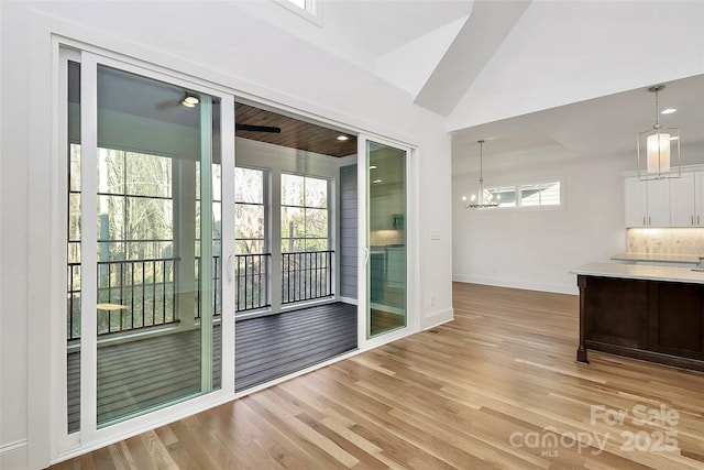 interior space with light countertops, vaulted ceiling, light wood-style flooring, an inviting chandelier, and white cabinets