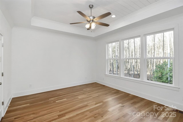 unfurnished room with a wealth of natural light, baseboards, a tray ceiling, and wood finished floors