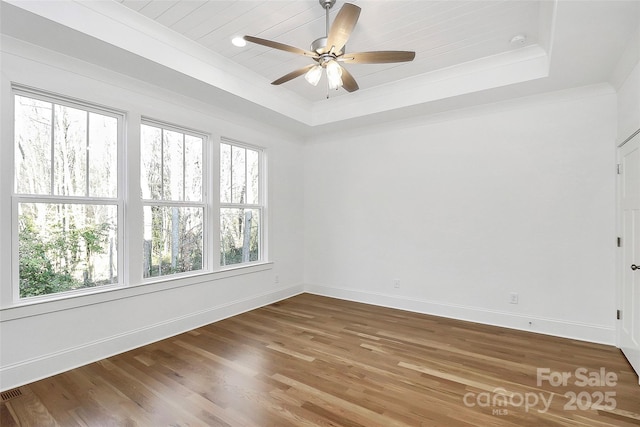 spare room featuring baseboards, a tray ceiling, ornamental molding, wood finished floors, and a ceiling fan