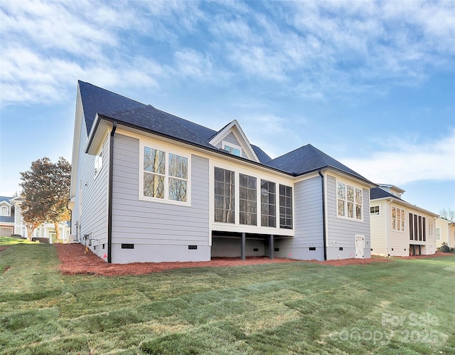 rear view of house featuring a shingled roof, a lawn, and crawl space