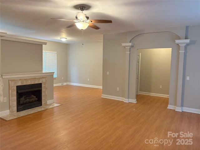 unfurnished living room featuring decorative columns, a fireplace, light wood-type flooring, and ceiling fan