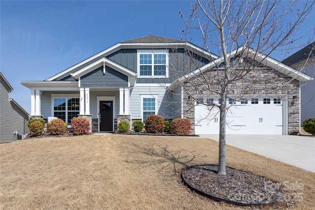 craftsman-style house featuring a front yard, driveway, a garage, stone siding, and board and batten siding