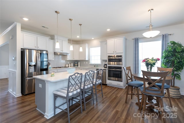 kitchen with visible vents, under cabinet range hood, a kitchen island, white cabinetry, and appliances with stainless steel finishes