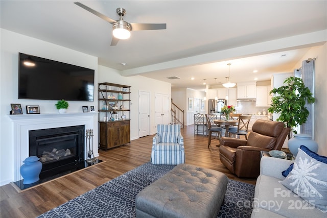 living area with stairway, dark wood-type flooring, visible vents, and a ceiling fan