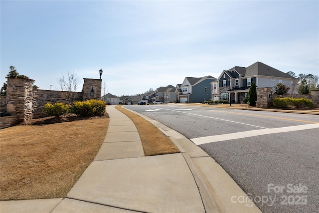 view of road with sidewalks, a residential view, curbs, and street lighting