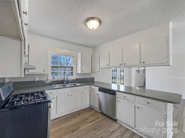 kitchen featuring a sink, dark countertops, white cabinetry, appliances with stainless steel finishes, and light wood finished floors