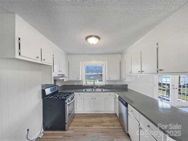 kitchen with dark countertops, under cabinet range hood, appliances with stainless steel finishes, white cabinets, and a sink