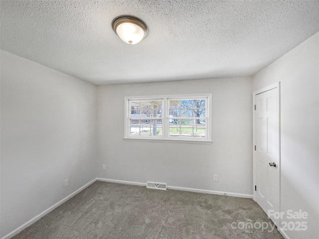 empty room with a textured ceiling, carpet, visible vents, and baseboards