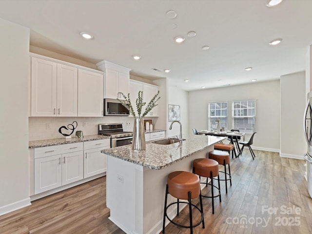 kitchen featuring a sink, stainless steel appliances, tasteful backsplash, and light wood-style floors