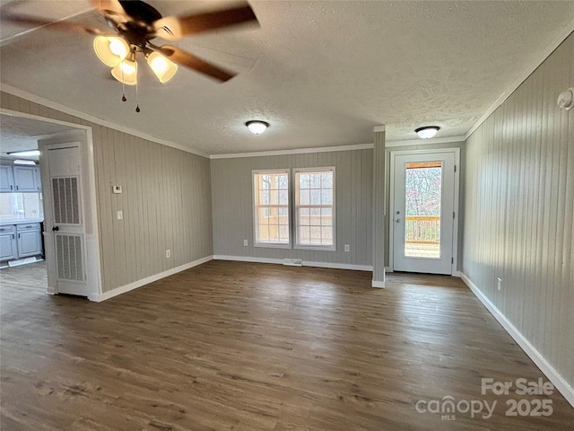 unfurnished living room featuring baseboards, dark wood finished floors, ornamental molding, a textured ceiling, and a ceiling fan