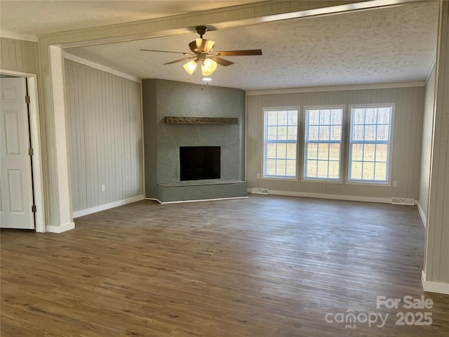 unfurnished living room with a fireplace with raised hearth, baseboards, dark wood-style floors, a textured ceiling, and a ceiling fan