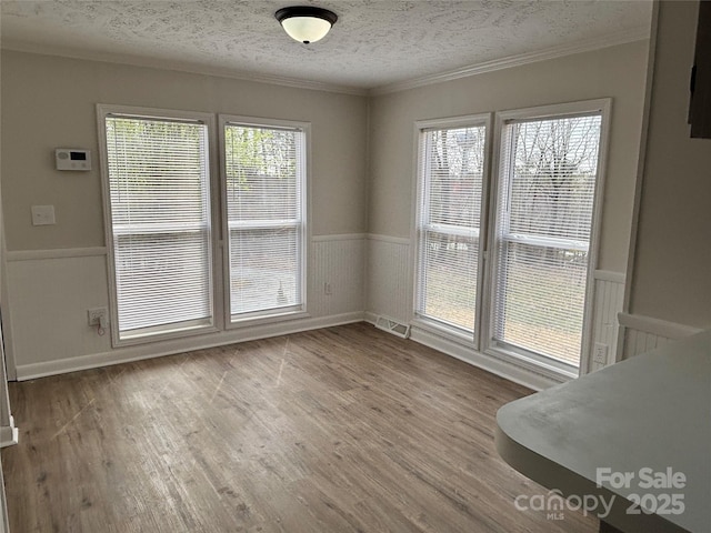 unfurnished dining area featuring a textured ceiling, wood finished floors, and wainscoting