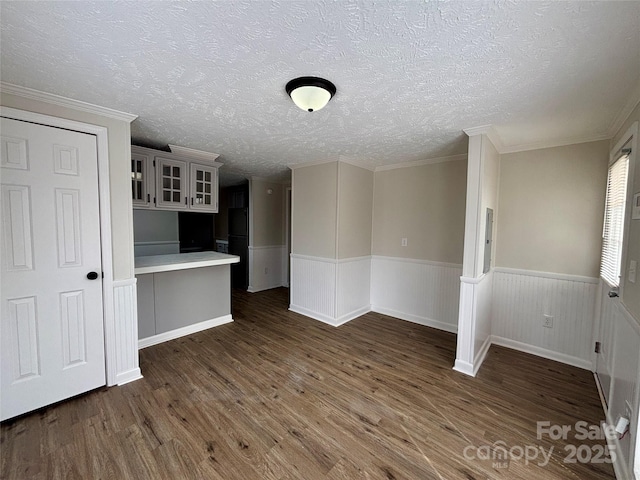 interior space featuring a textured ceiling, ornamental molding, wood finished floors, and wainscoting