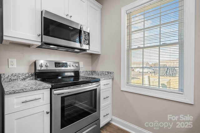 kitchen with dark wood finished floors, stainless steel appliances, white cabinets, baseboards, and light stone countertops