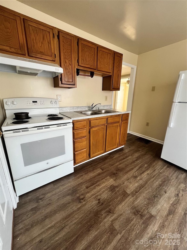 kitchen featuring dark wood-type flooring, under cabinet range hood, light countertops, white appliances, and a sink