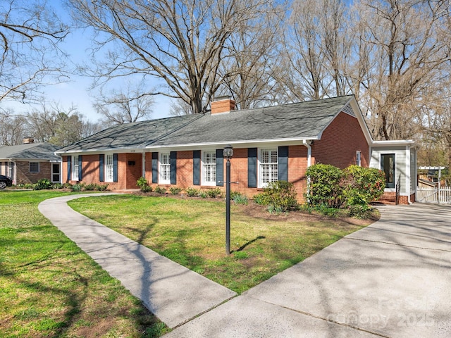 ranch-style home with a shingled roof, a front yard, brick siding, and a chimney