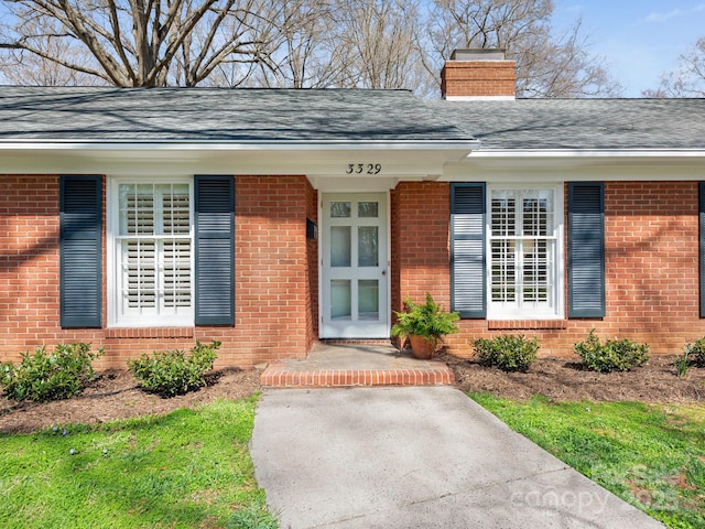 property entrance with a shingled roof, brick siding, and a chimney