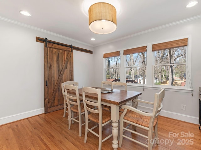 dining space with a barn door, crown molding, light wood-type flooring, and baseboards