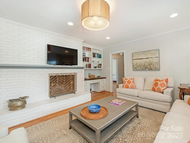 living area with a fireplace, crown molding, built in shelves, and wood finished floors