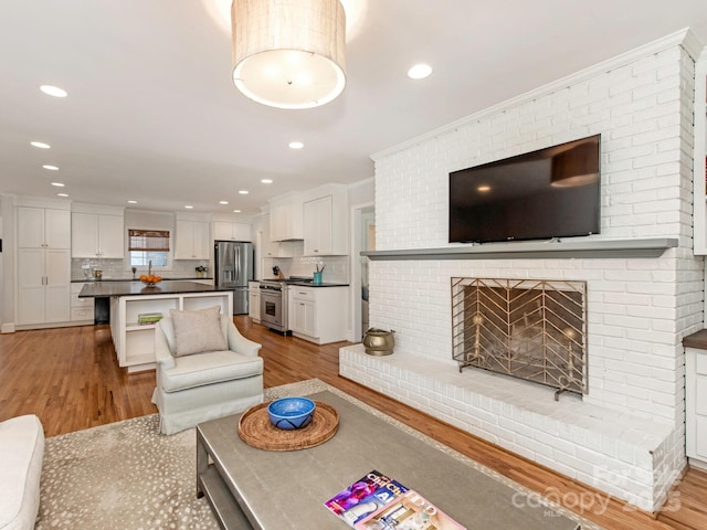 living area featuring light wood finished floors, recessed lighting, a fireplace, and crown molding