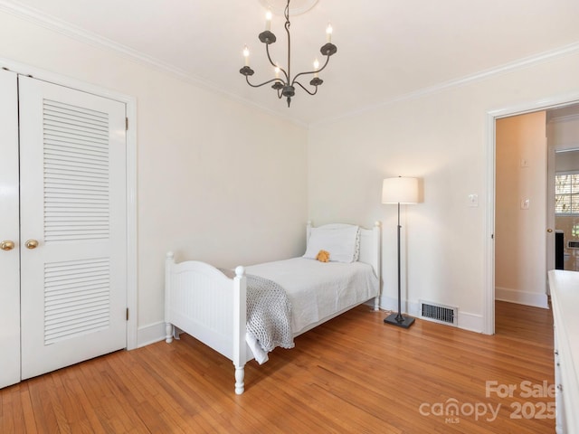 bedroom featuring visible vents, crown molding, light wood finished floors, baseboards, and a chandelier