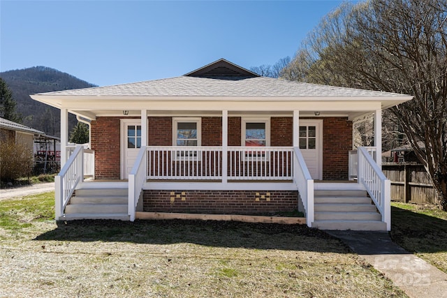 bungalow with a front yard, fence, covered porch, a shingled roof, and brick siding