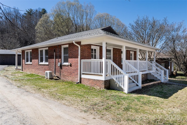 view of side of home featuring brick siding, a porch, a yard, and roof with shingles