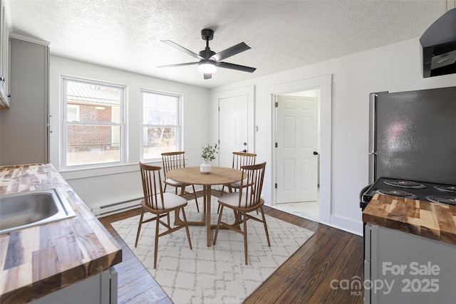 dining room featuring dark wood-type flooring, a ceiling fan, a textured ceiling, a baseboard radiator, and baseboards