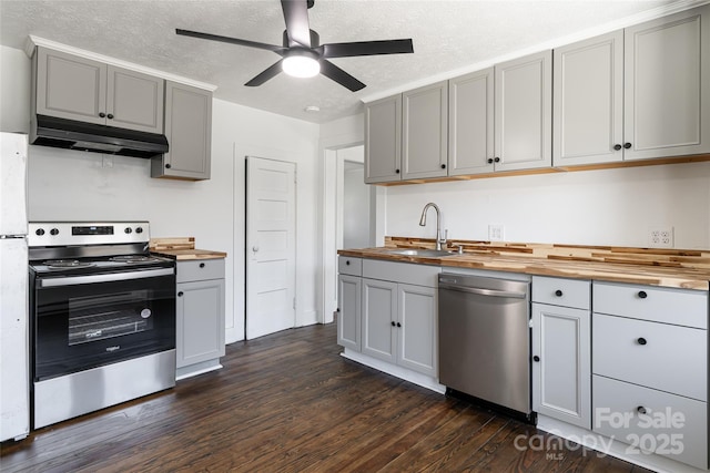 kitchen featuring under cabinet range hood, butcher block countertops, gray cabinets, and appliances with stainless steel finishes