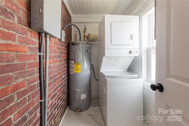 laundry room featuring brick wall, electric water heater, laundry area, stacked washing maching and dryer, and marble finish floor