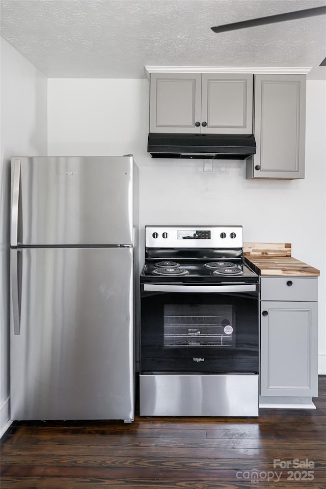 kitchen with gray cabinetry, dark wood-type flooring, under cabinet range hood, butcher block countertops, and stainless steel appliances