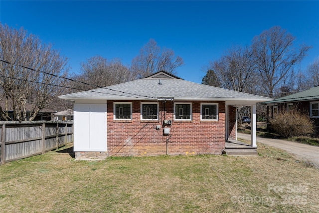 back of property featuring brick siding, a lawn, a shingled roof, and fence