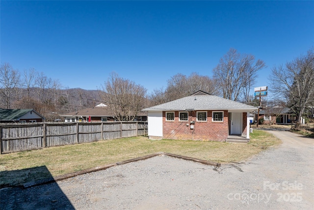 back of property featuring a yard, fence, brick siding, and roof with shingles