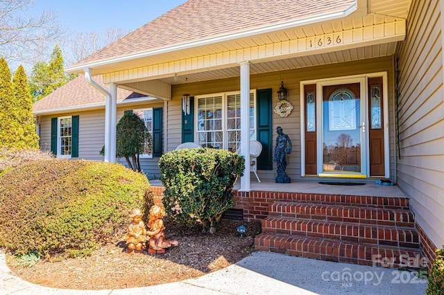 doorway to property featuring a porch and a shingled roof