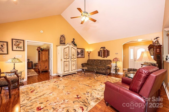 living room featuring wood finished floors, baseboards, high vaulted ceiling, arched walkways, and ceiling fan