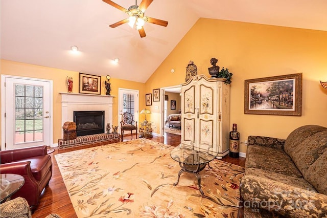 living area featuring baseboards, a fireplace, wood finished floors, high vaulted ceiling, and a ceiling fan