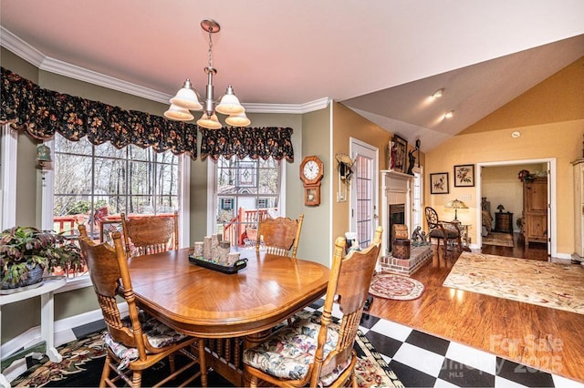 dining room with vaulted ceiling, a notable chandelier, a fireplace with raised hearth, and ornamental molding