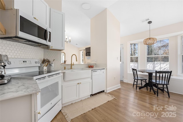 kitchen featuring visible vents, a sink, white appliances, light wood-style floors, and light countertops