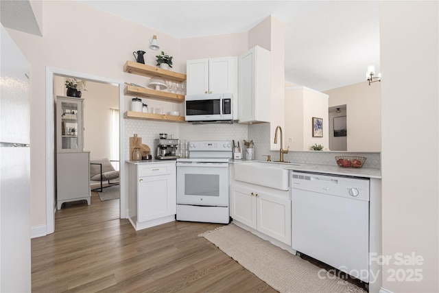 kitchen featuring tasteful backsplash, light countertops, light wood-style floors, white appliances, and a sink