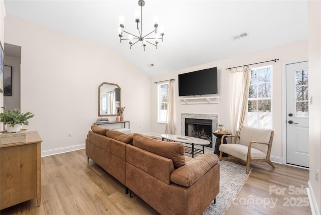 living area with light wood-type flooring, visible vents, a high end fireplace, a chandelier, and vaulted ceiling