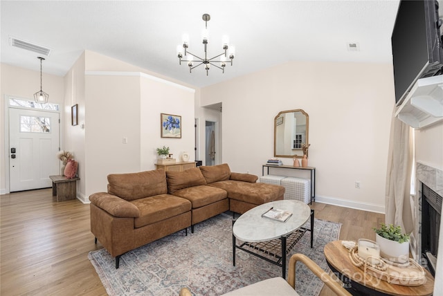 living room with visible vents, baseboards, a chandelier, vaulted ceiling, and light wood-style flooring