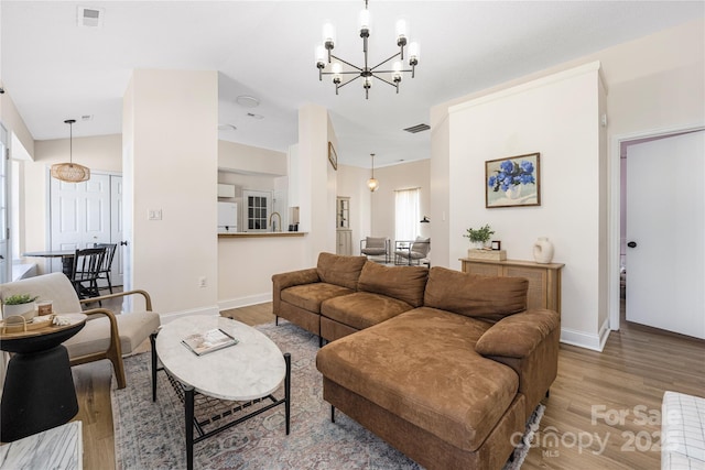 living room featuring visible vents, baseboards, a notable chandelier, and wood finished floors