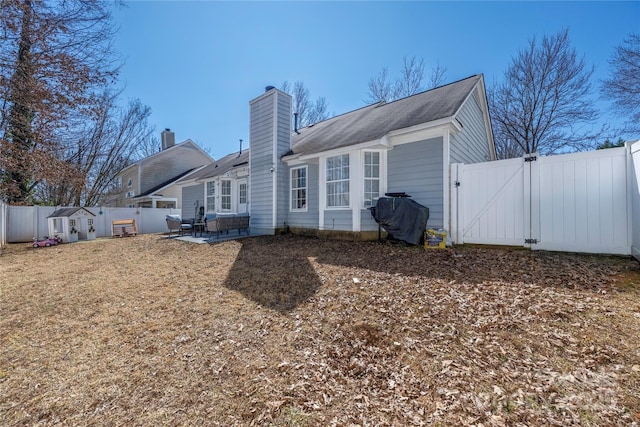 back of house featuring a patio area, a chimney, a fenced backyard, and a gate