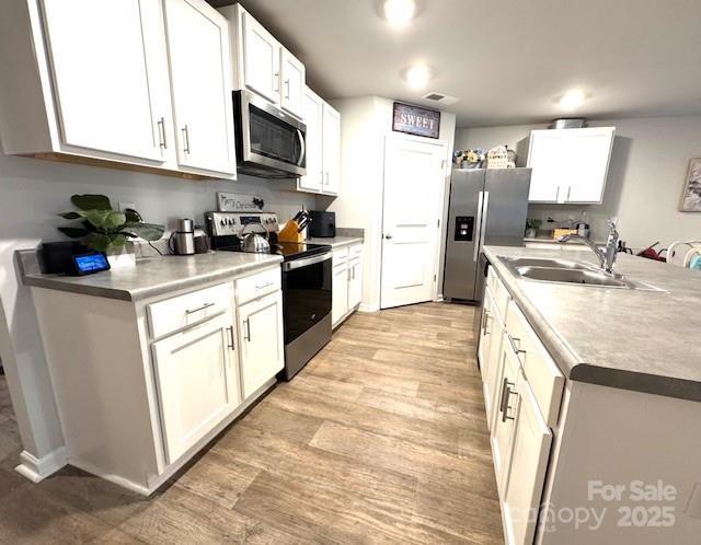 kitchen featuring appliances with stainless steel finishes, white cabinetry, light wood-style floors, and a sink