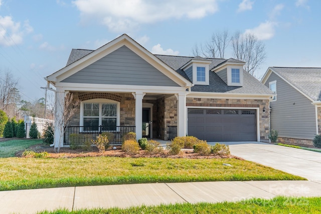 view of front of property with a front lawn, driveway, covered porch, roof with shingles, and a garage