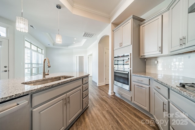 kitchen with visible vents, a sink, a tray ceiling, stainless steel appliances, and arched walkways